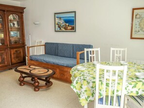 A cozy living room with a blue sofa, wooden cabinet, and a dining table with a lemon-patterned tablecloth.