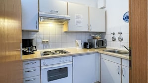A compact kitchen with white cabinets, a stove, a microwave, and a coffee maker.