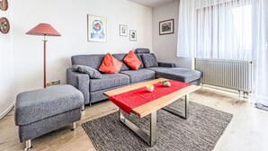 A modern living room with a grey sofa, red cushions, a wooden coffee table, and a red rug.
