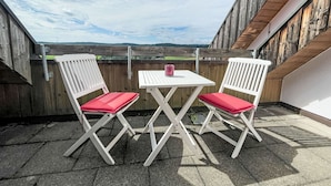 A patio with two white chairs and a table, overlooking a scenic view.
