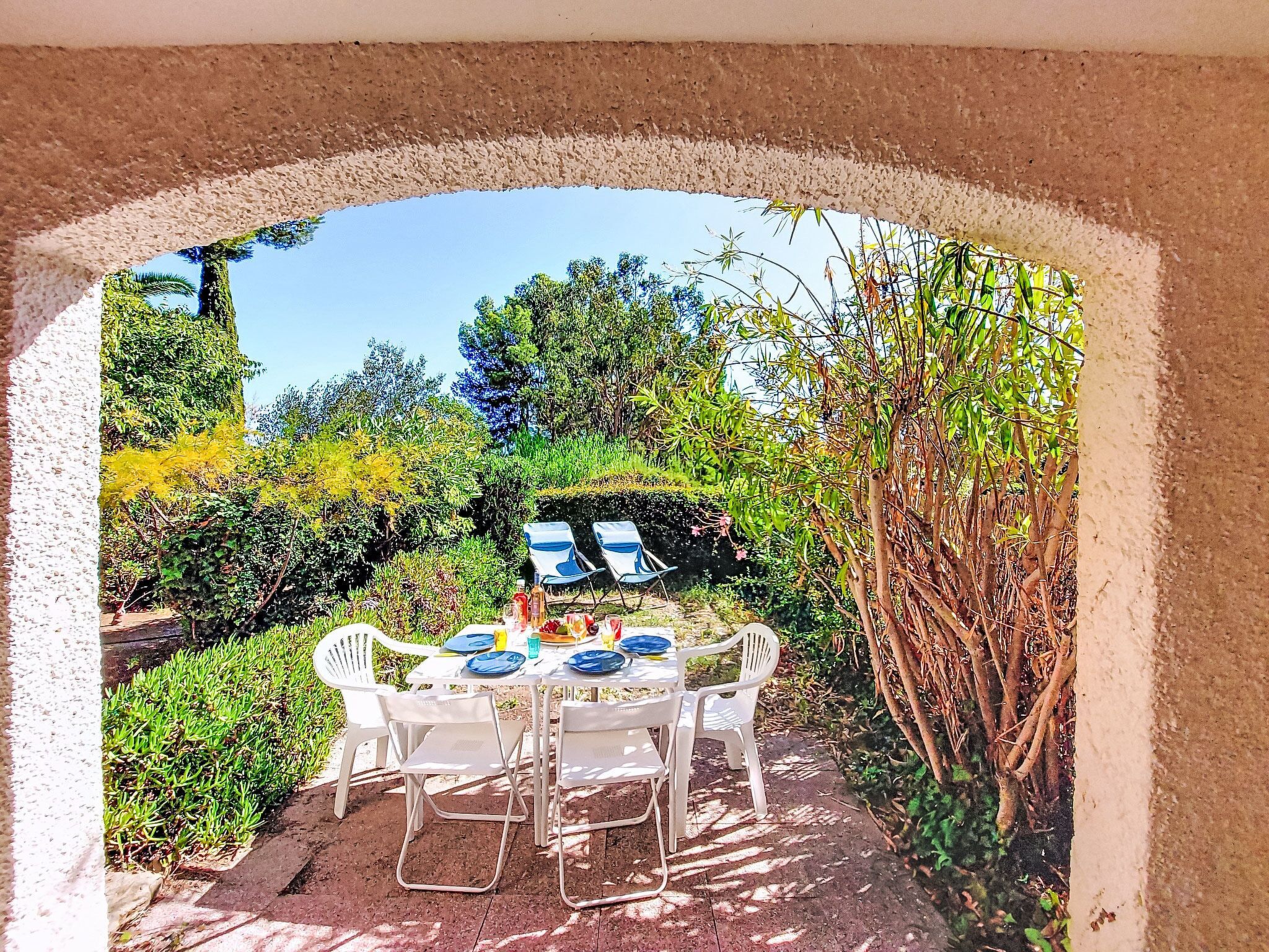 Eine Terrassengruppe im Freien mit Tisch und zwei Stühlen, umgeben von weißen Sitzgelegenheiten, unter einem steinernen Bogen.