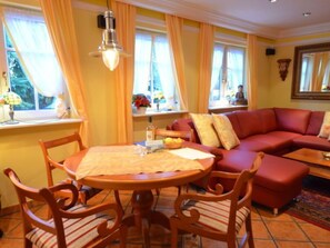 A cozy living room with a red sofa, wooden chairs, a round table, and a window with curtains. - Lotsenhaus by Interhome (Groß Zicker)
