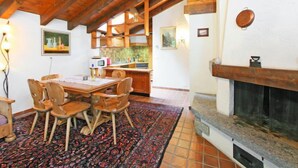 A rustic kitchen with wooden beams, a dining area with a patterned rug, and a fireplace. - Vitalis by Interhome (Zermatt)