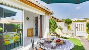 A patio with a round table set for dining, a small cabinet, and a door leading to a covered area. - Les Cristallines by Interhome (Cap d'Agde)
