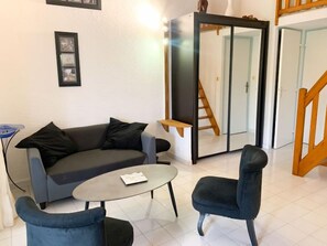 Ein modernes Wohnzimmer mit einem grauen Sofa, zwei Sesseln, einem Couchtisch und einer Treppe, die zu einer oberen Etage führt.