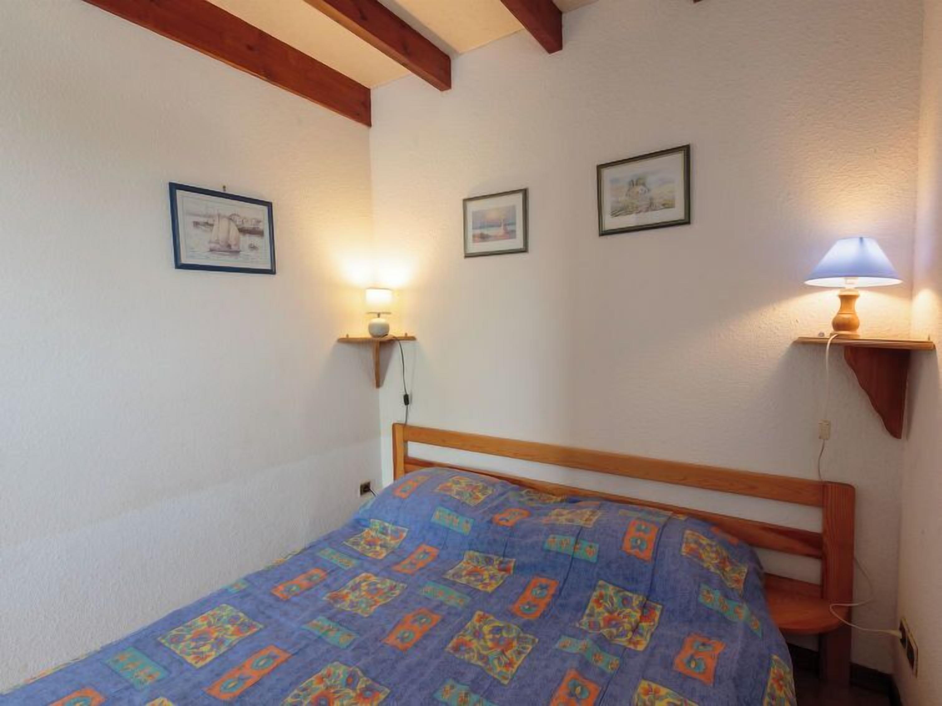 A small, cozy bedroom with a wooden bed, a blue patterned bedspread, and two wall-mounted lamps.