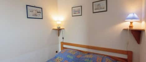 A small, cozy bedroom with a wooden bed, a blue patterned bedspread, and two wall-mounted lamps.