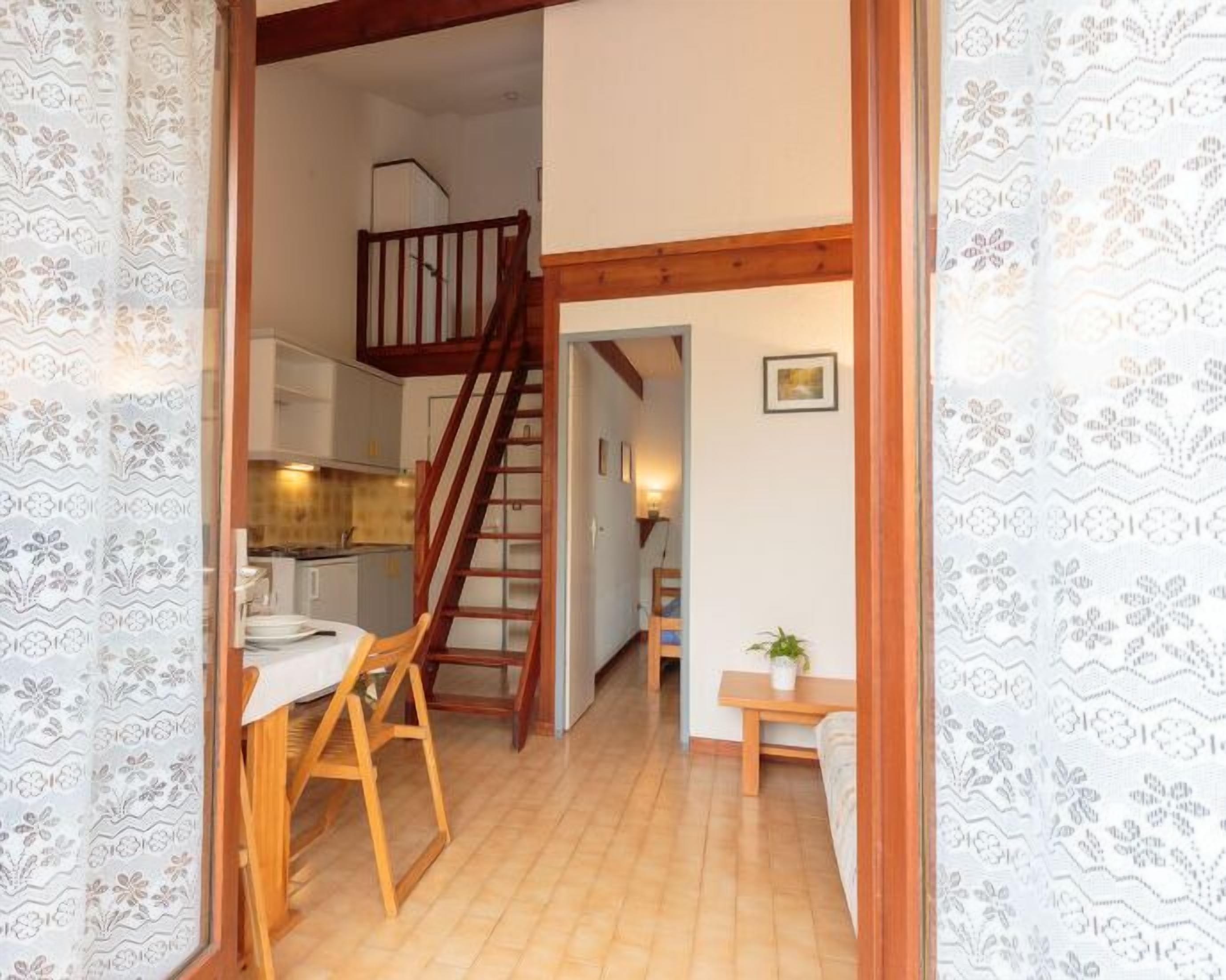 A staircase leading to a loft bedroom, a kitchen area, and a small seating area with a plant.