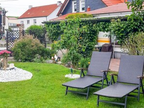 Ein Garten mit zwei Terrassenstühlen, einem kleinen Steingarten und einem Haus mit rotem Dach im Hintergrund.
