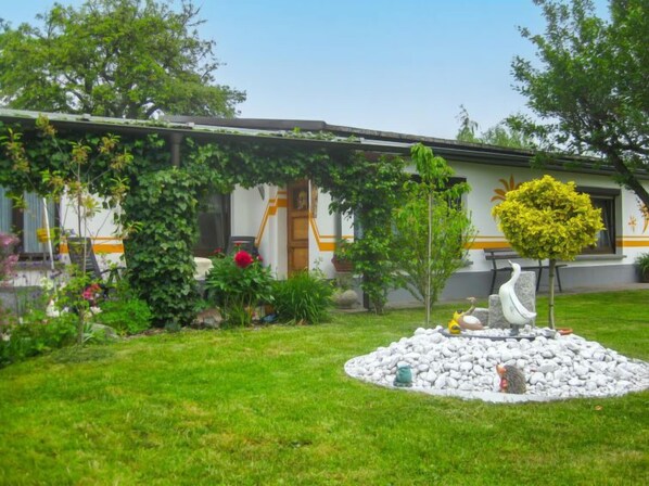 Ein Haus mit Garten, darin eine weiße Schwanstatue, ein kleiner Baum und ein Steingarten.