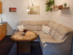 Ein Wohnzimmer mit einem beigen Sofa, einem Couchtisch und einer kleinen Küchenzeile mit Holzschränken.