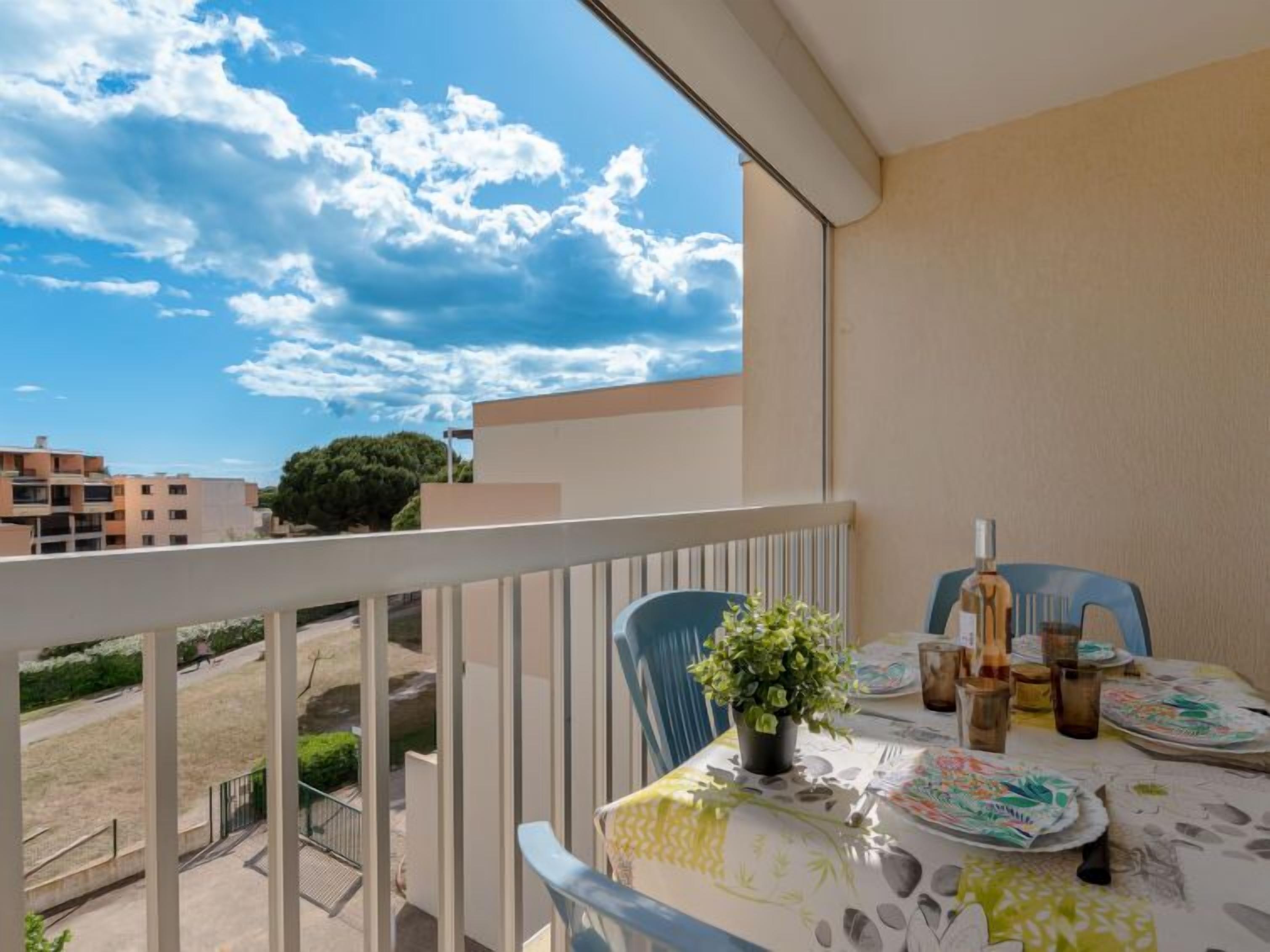 A balcony with a table set for dining, a potted plant, and a view of the sky and buildings.