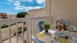 A balcony with a table set for dining, a potted plant, and a view of the sky and buildings. - Los Amigos by Interhome (Le Grau du Roi)
