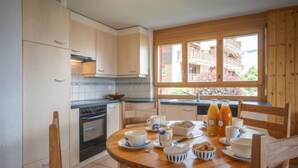 A modern kitchen with wooden cabinets, a stove, and a dining area with a table set for breakfast. - Seya 19 by Interhome (Ovronnaz)