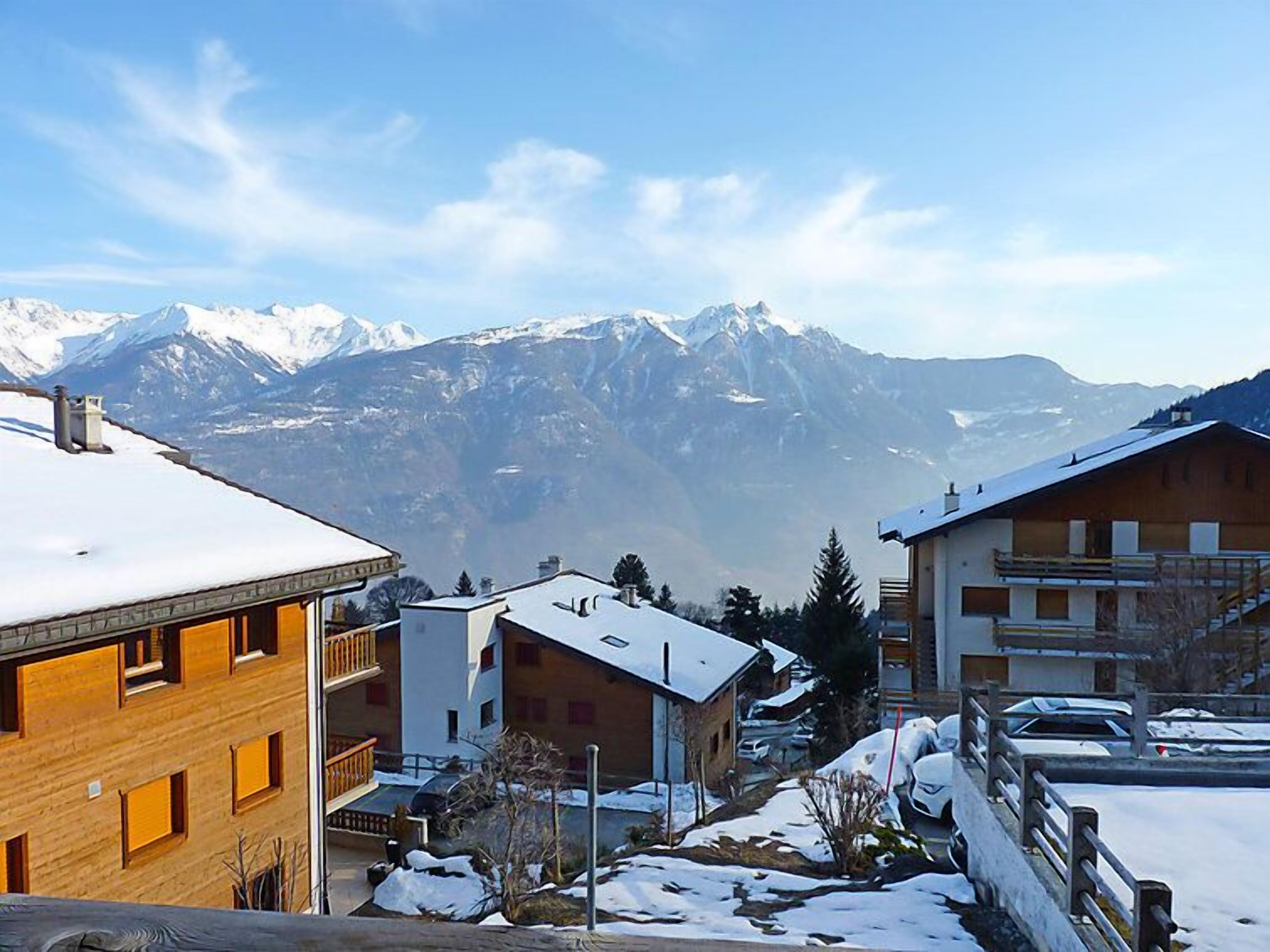 Un barrio residencial con tejados nevados y montañas al fondo.