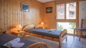 A wooden-paneled room with two beds, a window with a balcony view, and a hanging light fixture. - Seya 19 by Interhome (Ovronnaz)