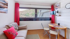 Una stanza accogliente e confortevole con divano, un tavolino, una sedia, una finestra vista su un paesaggio collinare e un televisore a parete.