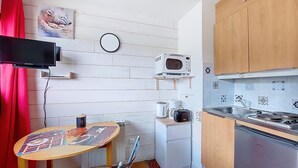 Una cucina compatta con forno a microonde, macchina del caffè e un piccolo frigorifero. C'è un tavolo da pranzo con un sottopiatti e una sedia.