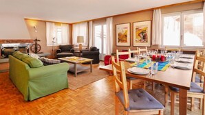 Amplia sala de estar con un sofá verde, una mesa de comedor para cuatro personas y una cocina al fondo.