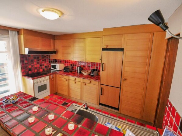 A compact kitchen with wooden cabinets, a microwave, a toaster, and a refrigerator.