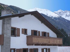 A two-story building with wooden balconies and a stone chimney, set against a backdrop of snow-capped mountains. - Vacation home Wiese by Interhome (Sankt Leonhard im Pitztal)