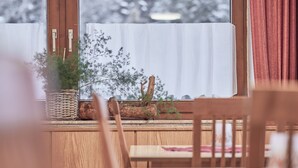 Un tavolo di legno con sedie, una finestra con tenda bianca e un vaso con piante sul davanzale.