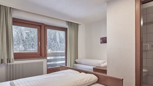 Una camera d'albergo con un letto, una finestra con tende, un termosifone e vista su alberi innevati.