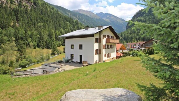 Un edificio a due piani con tetto piatto, immerso in un paesaggio montuoso e una fitta foresta.