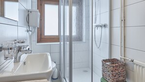 Un bagno moderno con cabina doccia in vetro, un lavandino bianco in stile classico e un piccolo sgabello con cesto intrecciato.