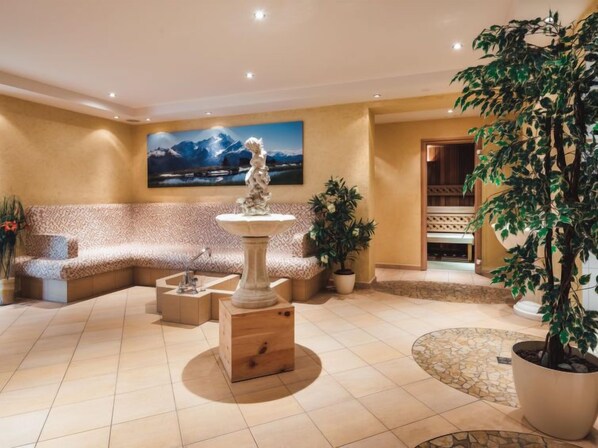 A spacious living room with a large sofa, a wooden coffee table, a decorative fountain, and a large potted plant.