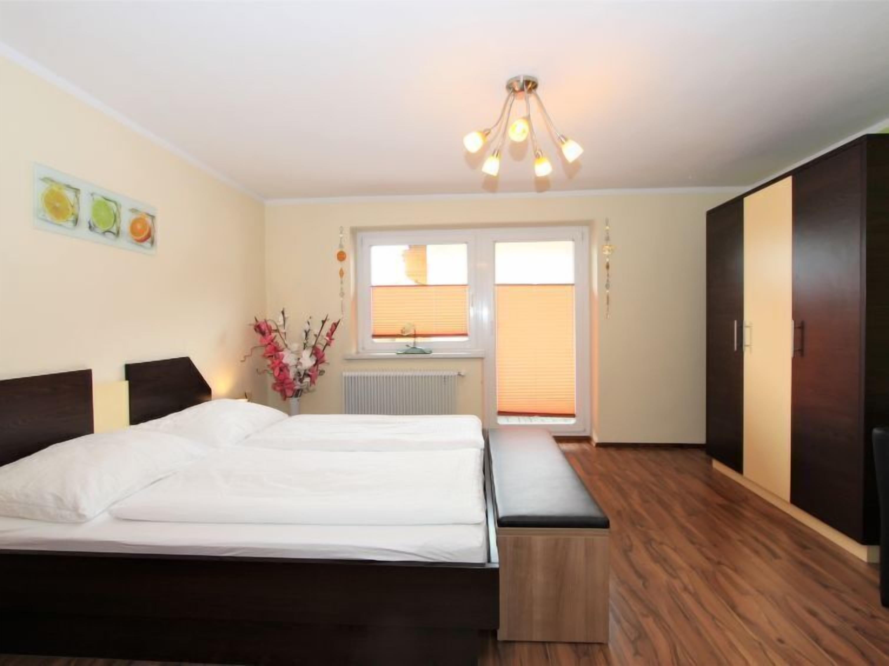 A bedroom with a large bed, a bench, a dresser, and a window with blinds.