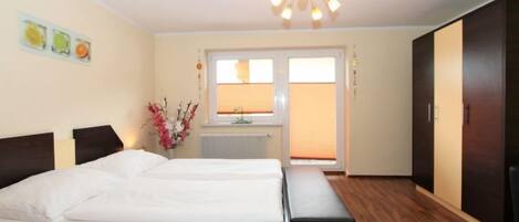 A bedroom with a large bed, a bench, a dresser, and a window with blinds.