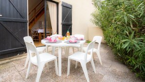 A round table with white plastic chairs, a small table with pink items, and a door with black shutters. - Les Maisons de la Plage by Interhome (Le Grau du Roi)