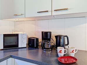 Una cocina moderna con microondas, tostadora, cafetera y hervidor sobre la encimera.