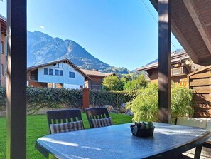 Eine Terrasse mit Tisch und Stühlen, Blick auf die Berge und ein Gebäude mit einem geneigten Dach.