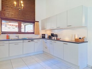 Eine moderne Küche mit weißen Schränken, einem Backofen und einem Fenster mit Vorhängen.