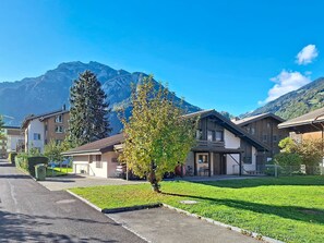 Eine Wohnstraße mit Häusern, einem Baum und Bergen im Hintergrund.