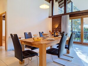 Un comedor con mesa de madera, sillas negras y vistas al exterior a través de ventanas grandes.