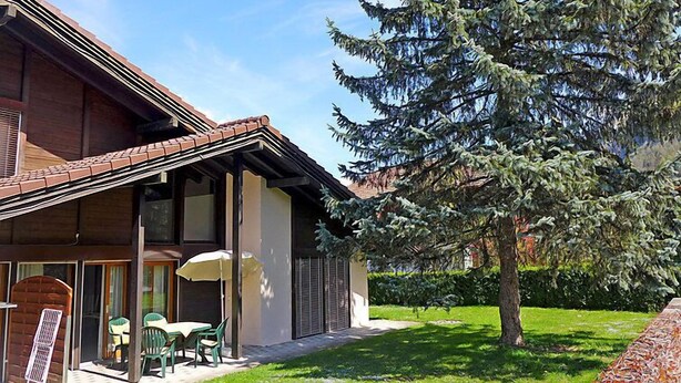 Un bâtiment à deux étages doté d’un patio couvert, d’un espace extérieur aménagé pour s’asseoir et d’un grand arbre à feuilles persistantes.