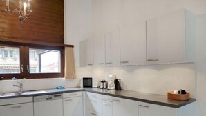 Une cuisine moderne avec des meubles blancs, un four à micro-ondes, une machine à café et une fenêtre avec des rideaux.