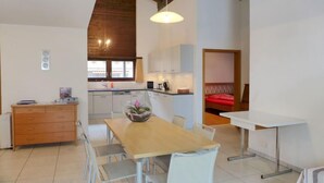 Une cuisine moderne avec des meubles blancs, une table à manger en bois et un luminaire suspendu.
