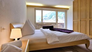Une chambre à coucher comprenant un lit, une table de chevet, une lampe, une fenêtre donnant sur un paysage verdoyant et une armoire en bois.