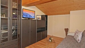 A cozy room with wooden beams, a TV on the wall, a sofa, and a small table with a bottle and glasses. - Voräule by Interhome (See)