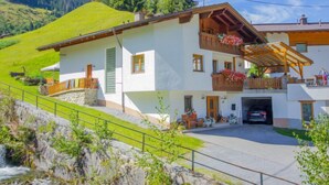 A two-story chalet with a stone foundation, wooden balconies with flower boxes, and a car parked in the driveway. - Voräule by Interhome (See)
