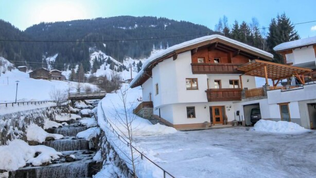 A two-story chalet with a wooden balcony, a stone wall, and a small waterfall in the foreground. - Voräule by Interhome (See)