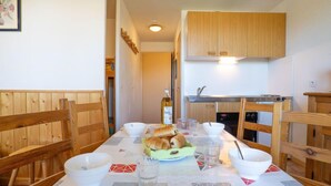Un coin repas avec une table en bois dressée pour deux personnes, une cuisine avec des placards en bois et un tableau encadré au mur.