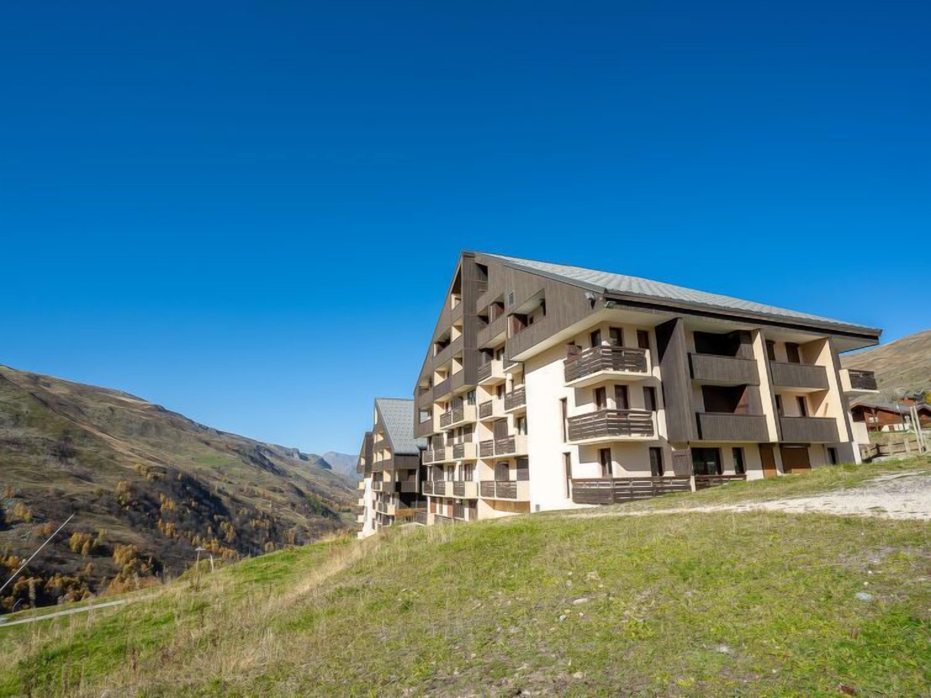 Un hotel de varios pisos con un diseño arquitectónico moderno, situado en una zona montañosa bajo un cielo azul despejado.