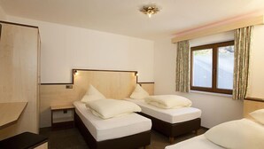 A hotel room with two single beds, a wooden headboard, a nightstand, a window with curtains, and a ceiling light fixture. - Apartment Alpin by Interhome (Sölden)