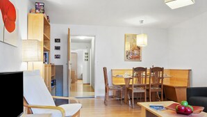 En kompakt opholdsstue med spiseplads, et fjernsyn og en bogreol.