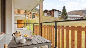 En balkon med et træbord, stole og en skål med frugt.
